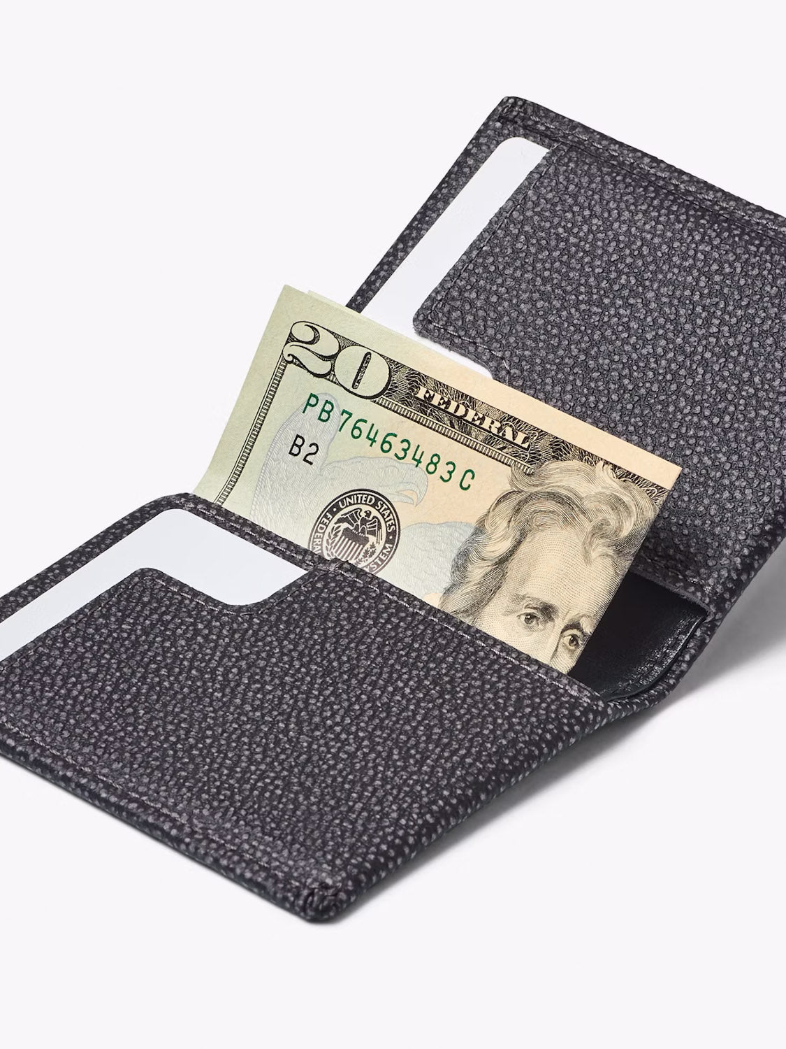 A Bellroy Slim Sleeve Wallet in black textured leather is open, revealing a U.S. twenty dollar bill and two white cards in its slots against a white background—designed for ultimate pocket friendliness.