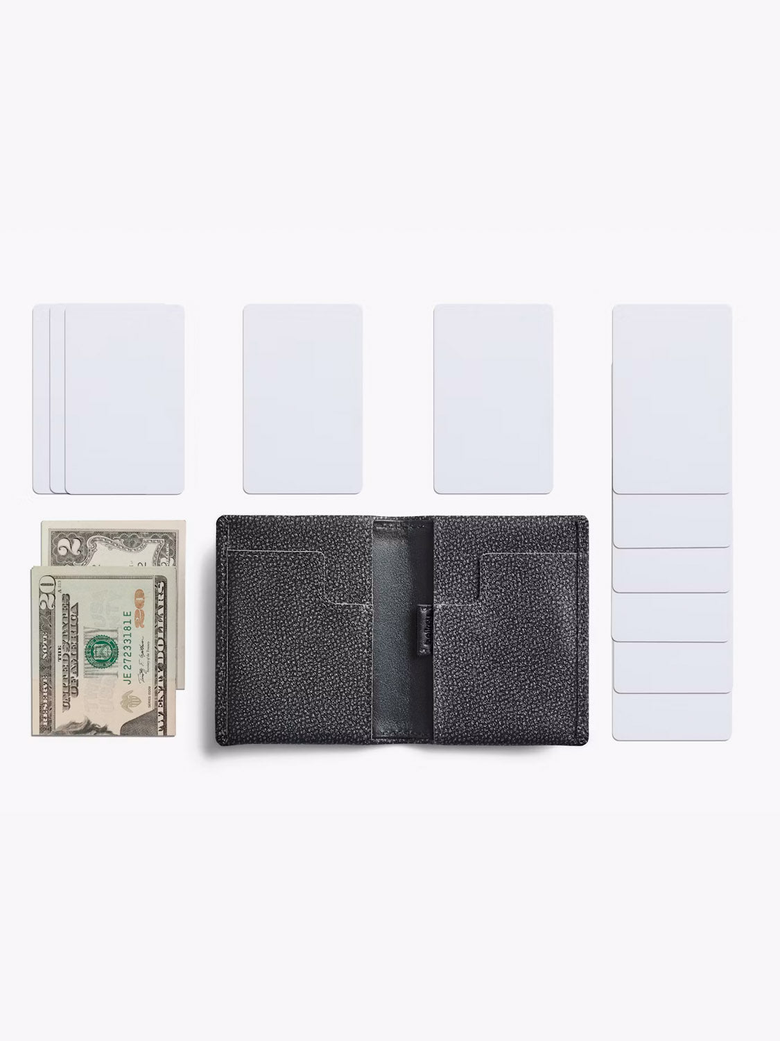 The Bellroy Slim Sleeve Wallet, shown open and empty in black leather, is surrounded by blank cards and U.S. dollar bills on a white background—showcasing a sleek, minimalist way to carry just your essentials.