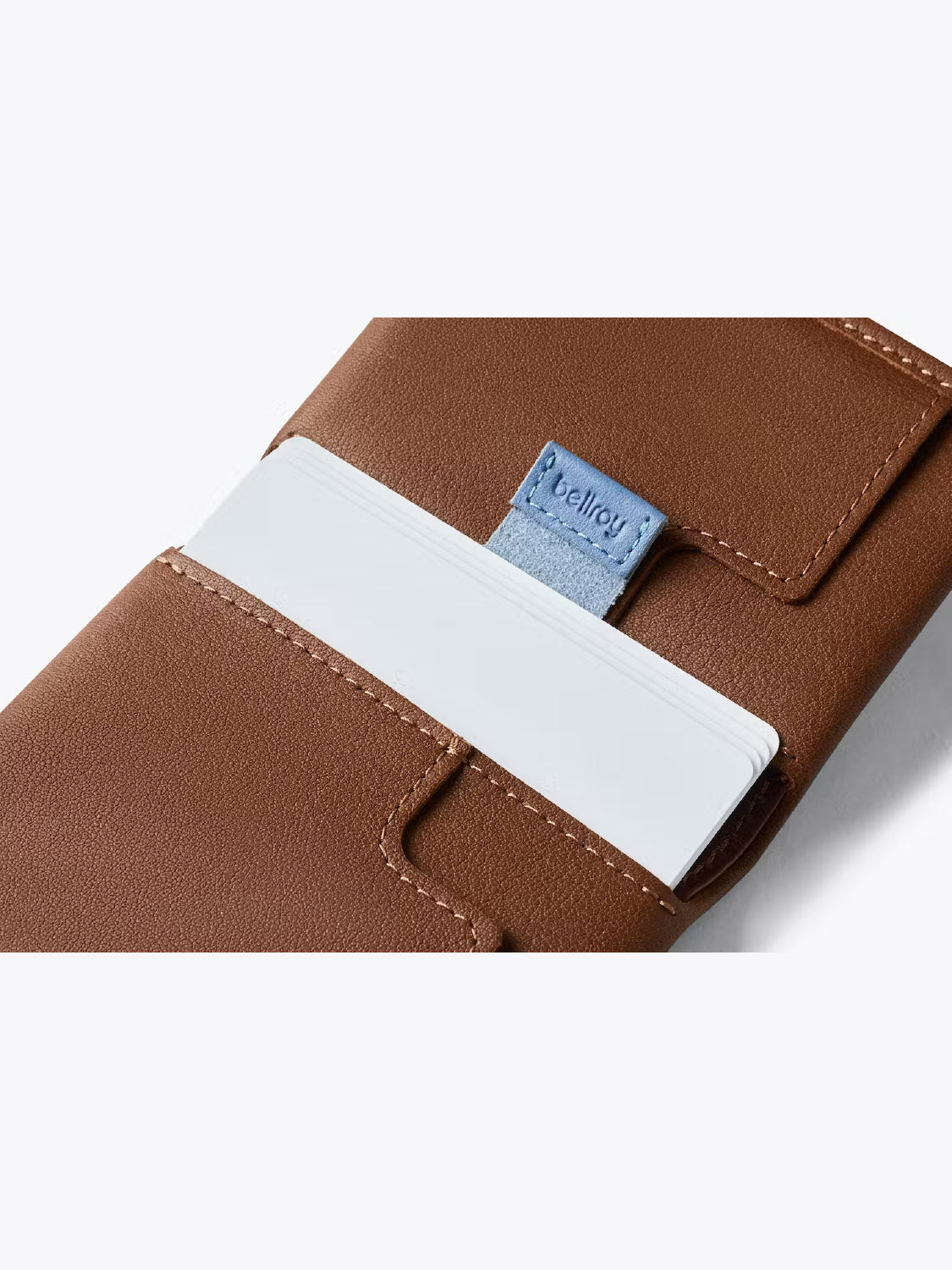 A close-up of the Bellroy Slim Sleeve Wallet in brown leather displays white cards neatly inside and a blue Bellroy tag, showcasing its pocket-friendly, slim design.