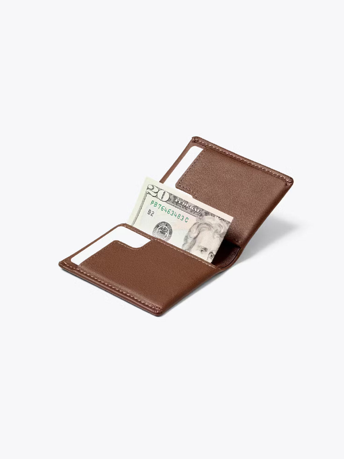 A Bellroy Slim Sleeve Wallet in brown is open on a plain light background, showing a folded twenty-dollar bill and an empty card slot.