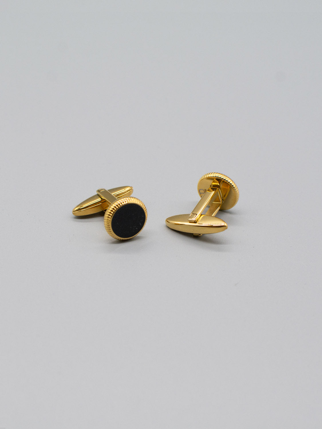 On a light gray background, two Gold Plated Steel Enamel Cufflinks by ID Menswear are showcased, featuring gold plating and black enamel inlays with a textured edge that adds sophistication, perfect for formal attire.