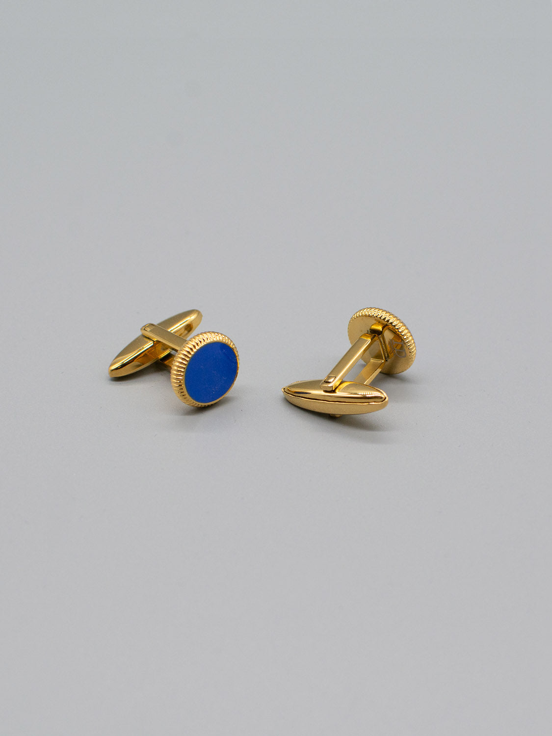 The Gold Plated Steel Enamel Cufflinks by ID Menswear feature round blue enamel inlays set against a gray background, making them perfect for formal attire.
