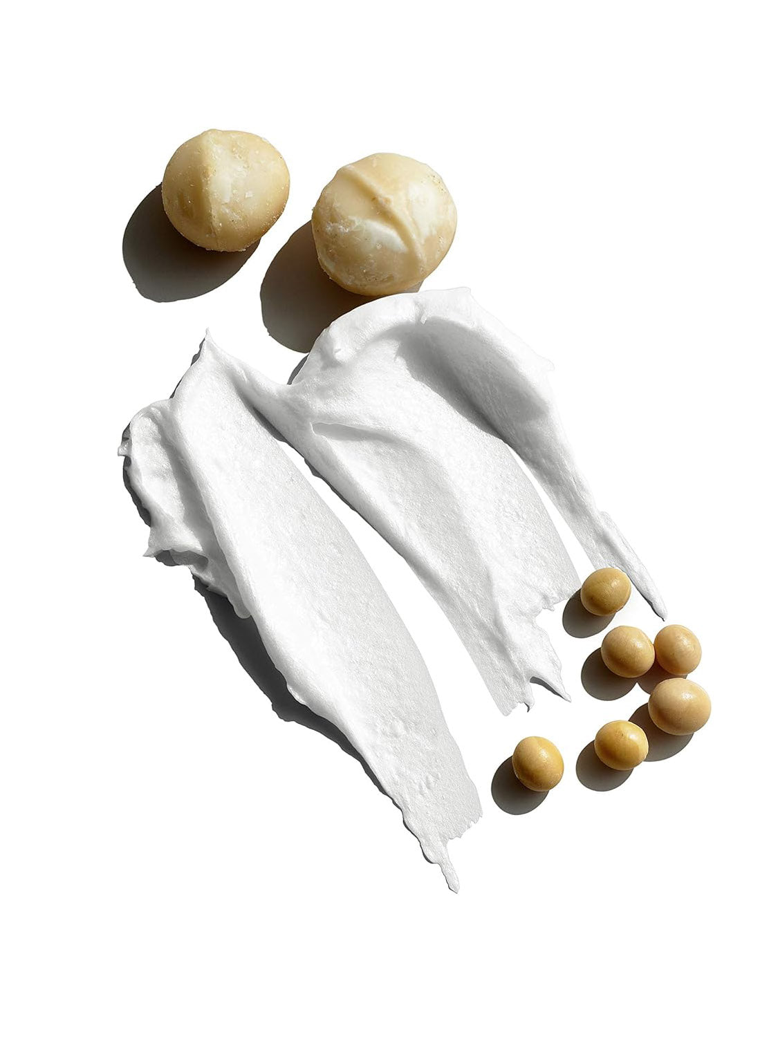 Two macadamia nuts, two smears of Jack Black Supreme Cream Triple Cushion Shave Lather, and six small round beige capsules are arranged on a white background, conveying a hydrating shave with reduced razor burn.