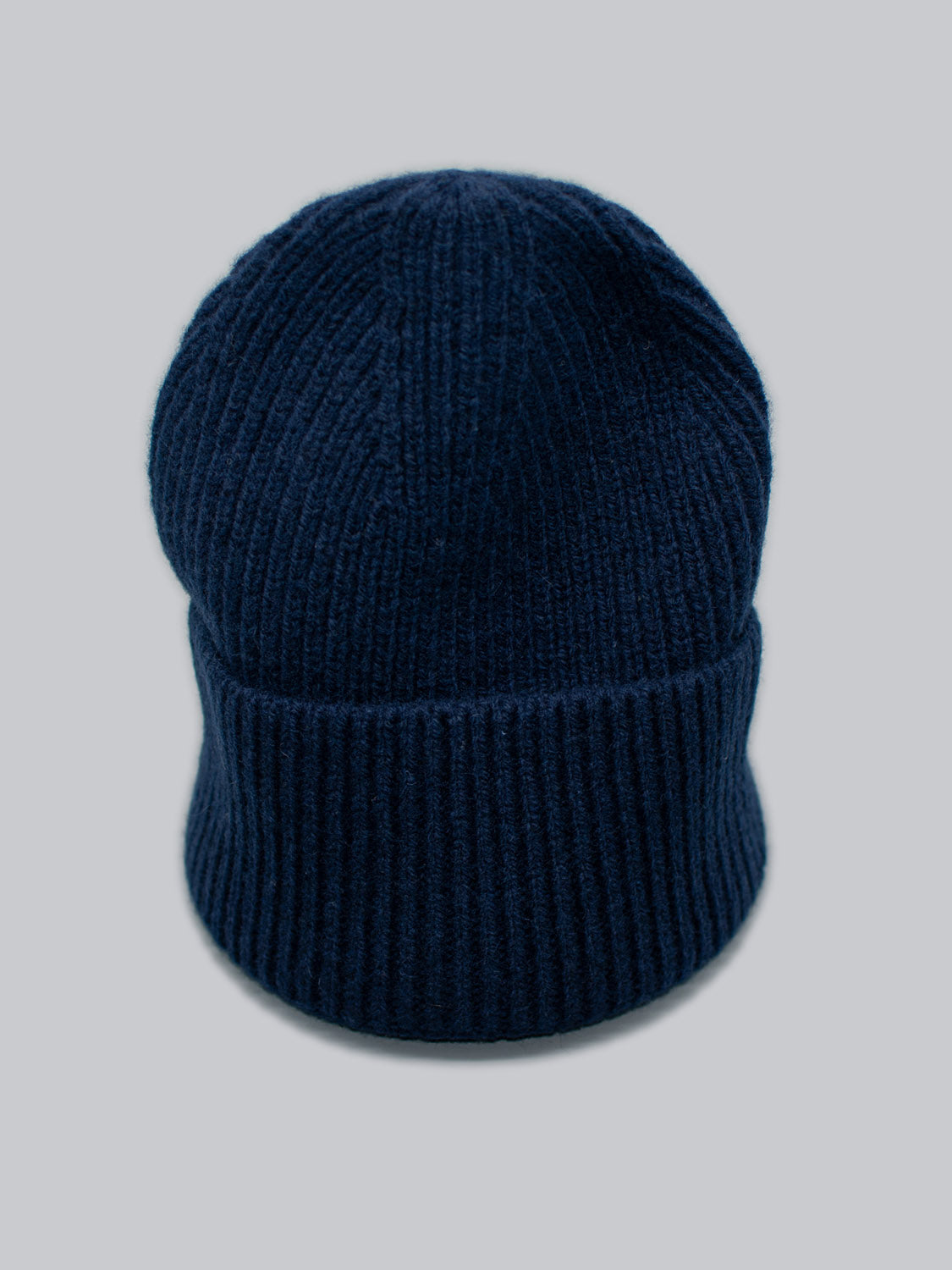 The Telluride Wool Beanie by ID Menswear features a navy blue, ribbed knit design, offering a comfortable fit and natural insulation against a light grey background.