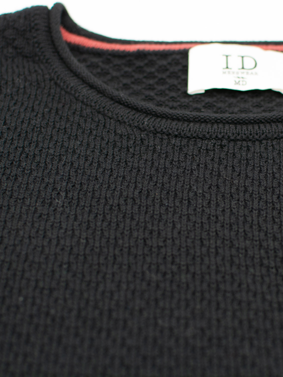 Close-up of a black textured Westside Rolled Crew Neck Sweater by ID Menswear, featuring a white label marked ID and MD and red piping inside. Part of our exclusive knitwear collection.