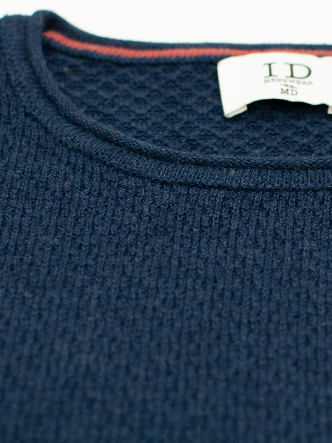 Close-up of the textured navy Westside Rolled Crew Neck Sweater by ID Menswear, featuring a red trim along the neckline. The medium-sized label inside denotes its place in our knitwear collection, highlighted by a waffle knit pattern.