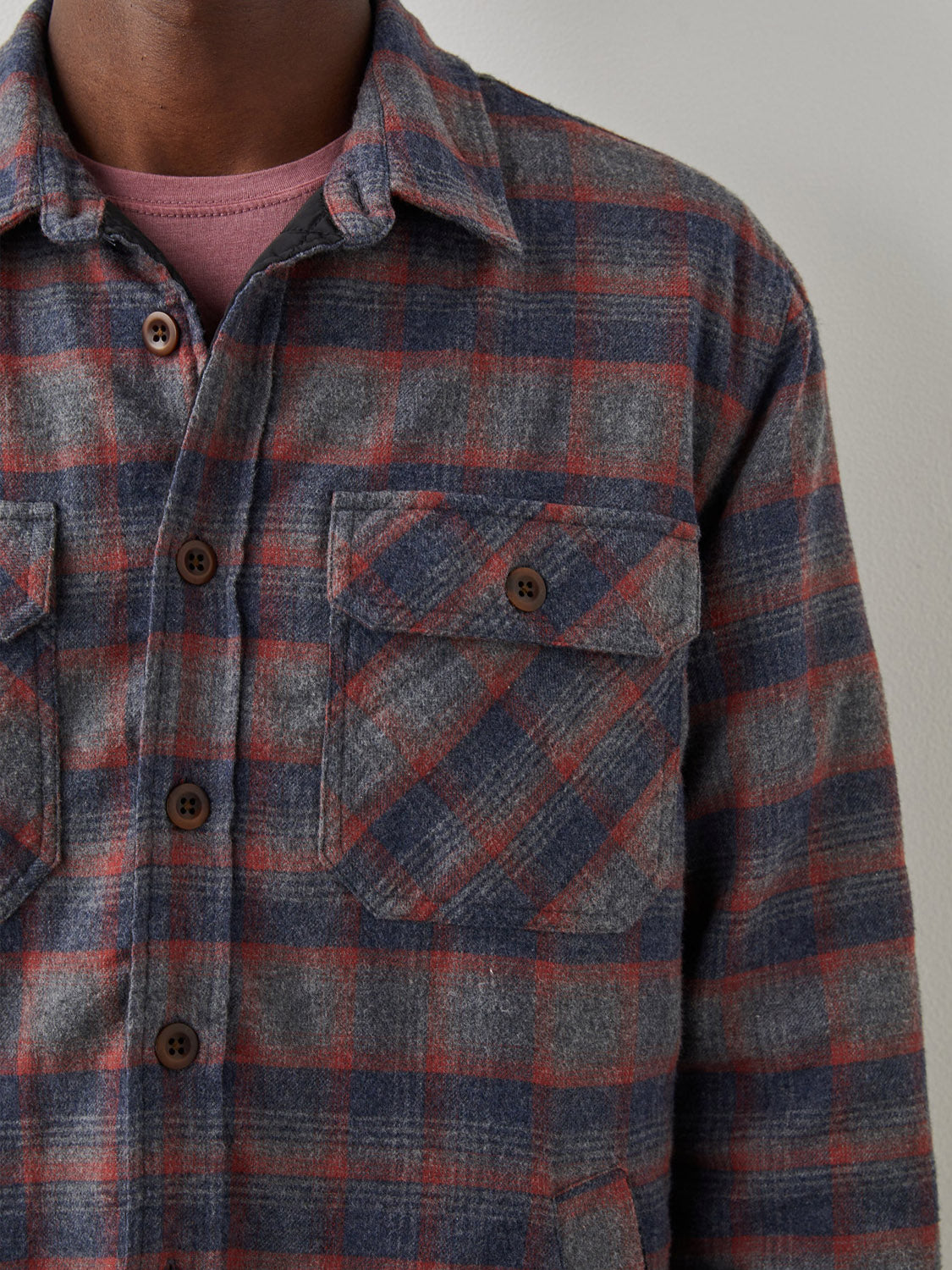 A person wearing the Rails Worthing Jacket, a plaid brushed cotton flannel in gray, red, and blue with brown buttons and two chest pockets, layered over a mauve t-shirt. Only the upper torso is visible in the image.