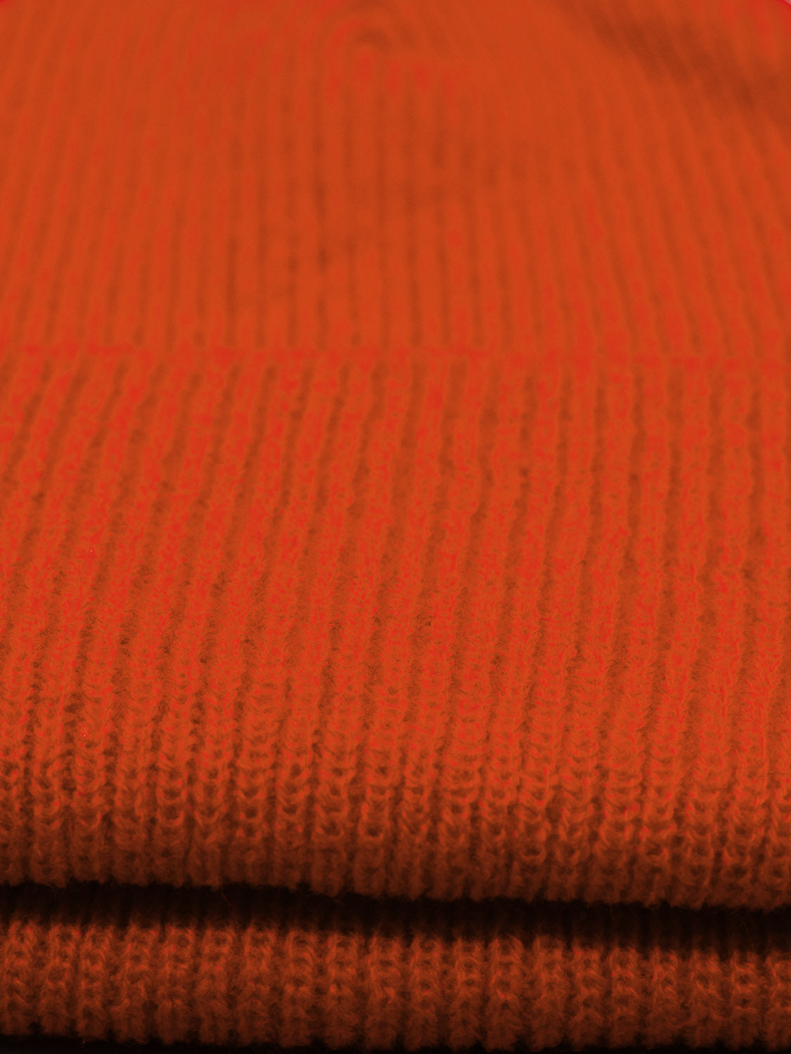 Close-up of a neatly folded bright orange acrylic knit fabric with ribbed texture, reminiscent of a classic fisherman style. Made by ID Menswear, this Yonker Ribbed Acrylic Beanie material has a cozy appearance ideal for crafting snug beanies.