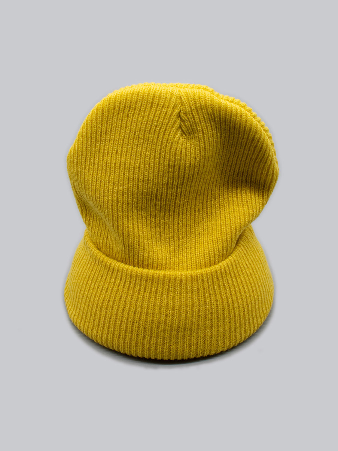 The Yonker Ribbed Acrylic Beanie from ID Menswear, in vibrant yellow and fisherman-style with a folded brim, is displayed against a plain gray background.