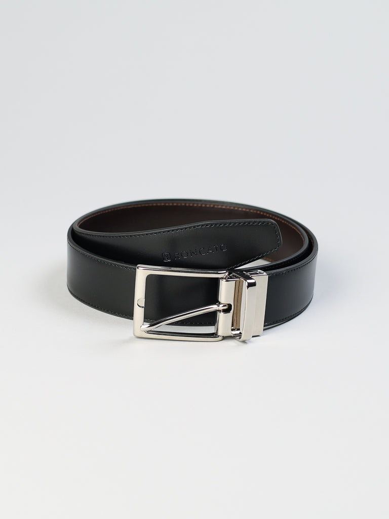 The 4026 Made in Italy Reversible Leather Belt by ID Menswear is elegantly coiled on a light gray background. It features a shiny silver buckle and a subtly embossed brand name near the end. The smooth black exterior contrasts beautifully with the genuine leather interior in a different shade.