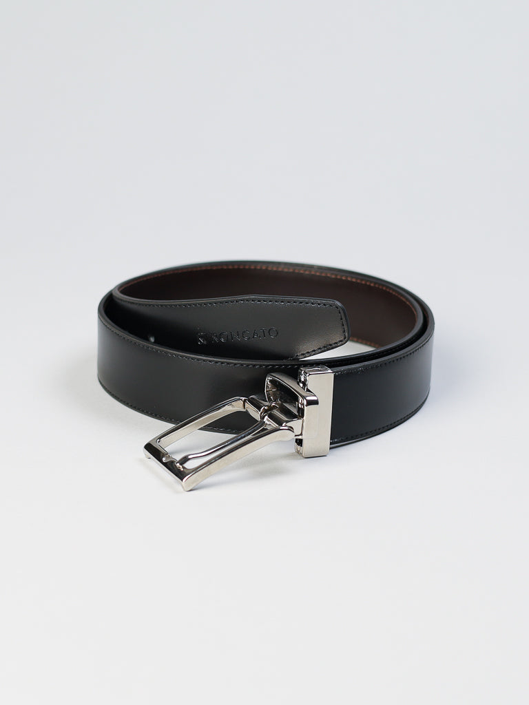 The 4026 Made in Italy Reversible Leather Belt by ID Menswear is coiled neatly on a light background, featuring a sleek metal buckle. Crafted from genuine leather, it boasts a subtle embossed pattern for a refined appearance.