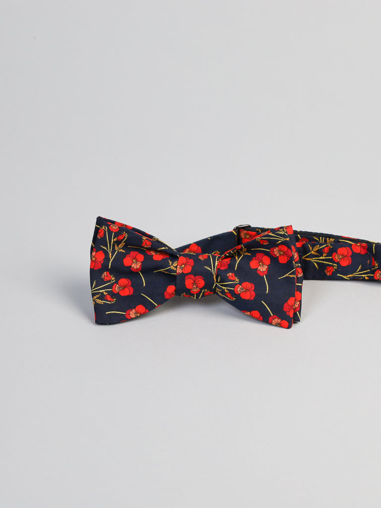 The ID Liberty of London Tana Lawn™ Poppy Red Cotton Bowtie by ID Menswear features a pattern of red poppy flowers on a light gray background. Handmade in Brooklyn, this silk-like piece is neatly tied, highlighting its refined craftsmanship.