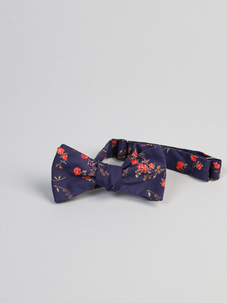 The ID Menswear navy bow tie features a floral pattern with red flowers and green leaves on a light gray backdrop. Made from Liberty of London Tana Lawn™ cotton, this piece is expertly handcrafted in Brooklyn.