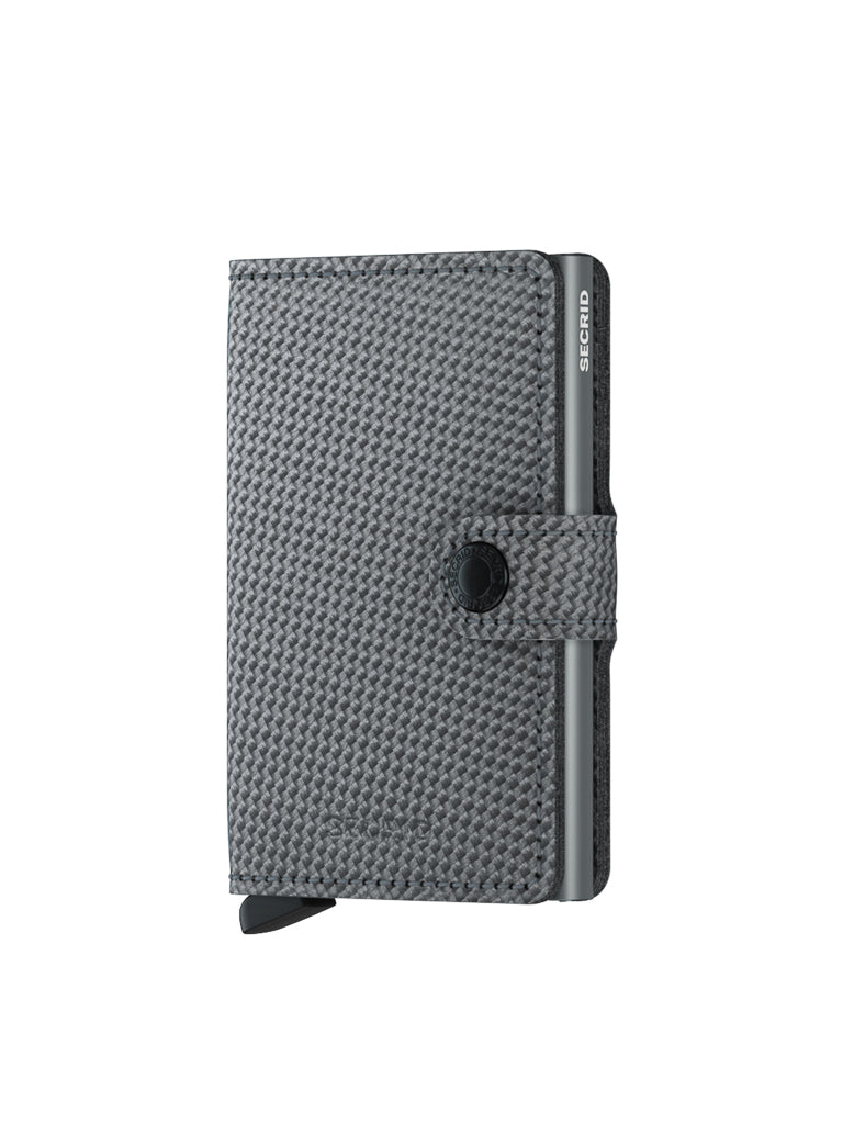 The Secrid Miniwallet Carbon Weave Pattern Leather is a compact gray wallet with RFID protection, a woven texture, snap closure strap, SECRID metal edge, and a black lever at the base. It stands upright on a white background.