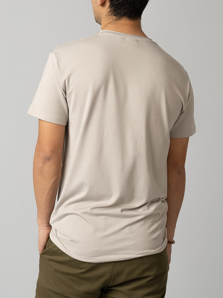 Back view of a person wearing the Bello Bamboo Blend Rolled Neck Tee from ID Menswear in beige and olive green pants, standing with hands in pockets against a plain gray background, showcasing sustainable clothing.