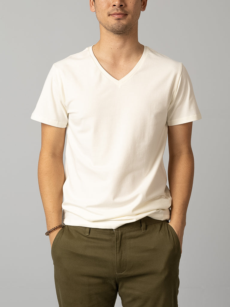 A person wearing a form-fitting Form V Neck Tee by ID Menswear and olive green pants stands against a plain gray background. Perfect for casual occasions, their hands rest in their pockets with a minimal bracelet on one wrist. The face remains unseen.
