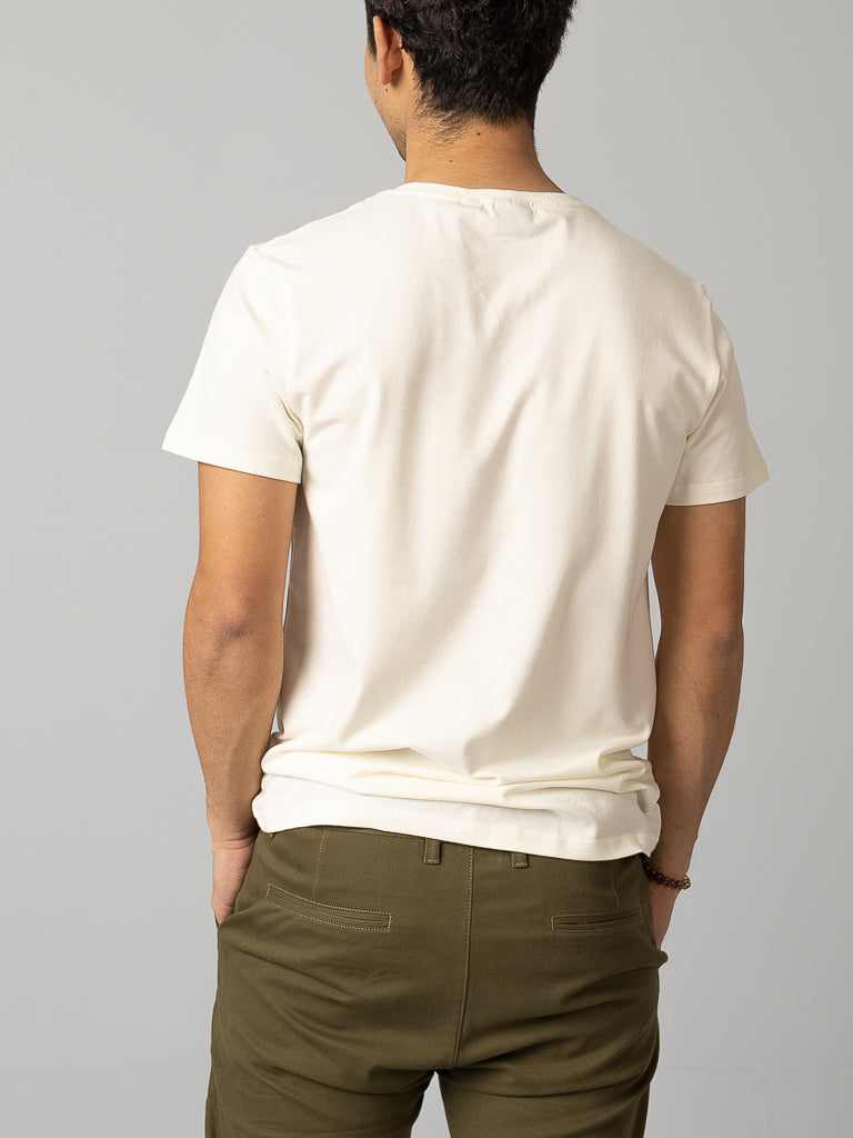 A person with short dark hair, turned away from the camera, wears an ID Menswear Form V Neck Tee in white and olive green pants. This outfit is ideal for a casual occasion against a plain gray background.