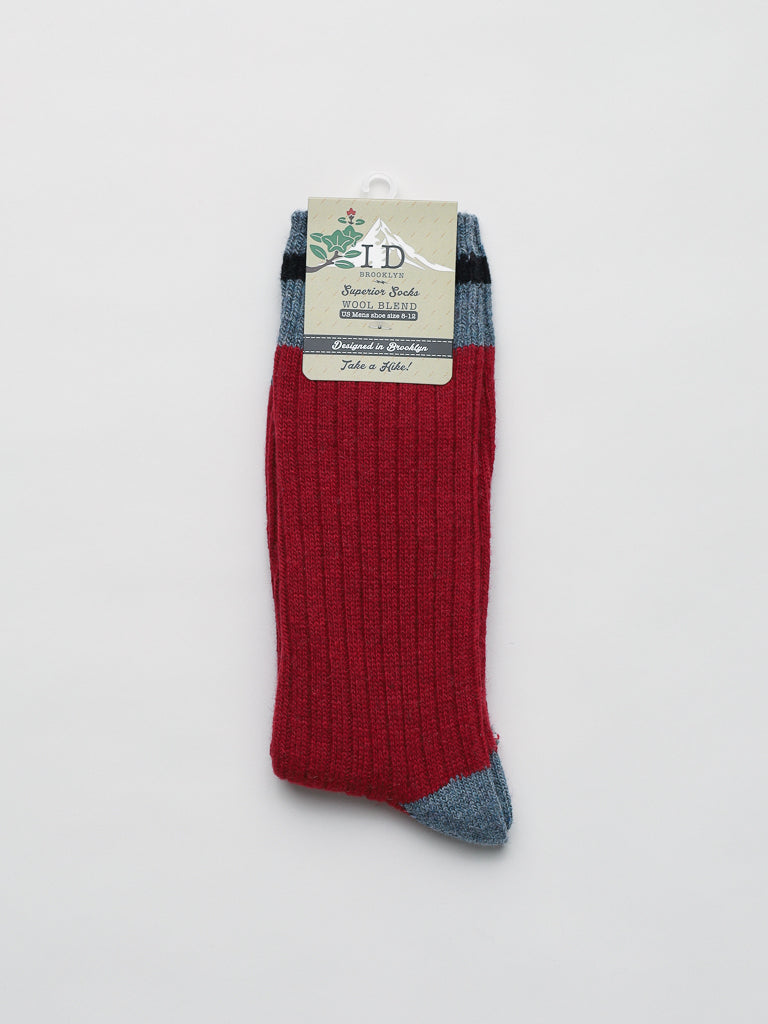 This single red Wool Blend Sock by ID Menswear features blue-gray toe and cuff details, a ribbed design perfect for winter activities, and is attached to a product label with a circular hole for hanging. Displayed against a plain white background.