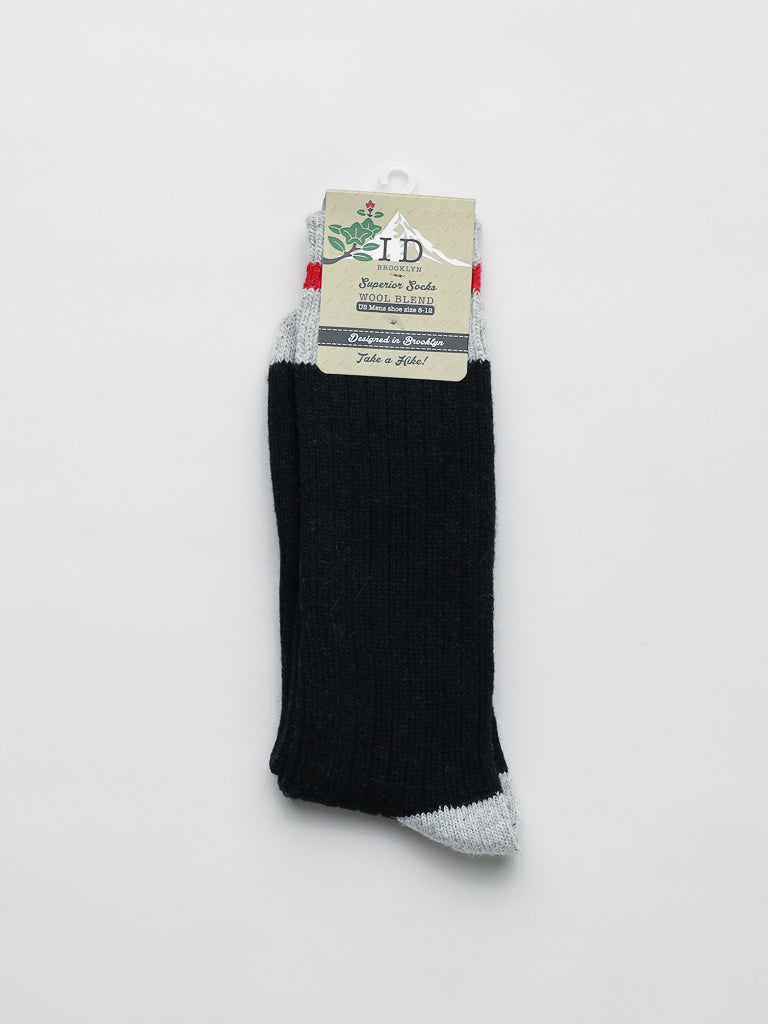 A black wool blend sock with light gray toe and heel accents from ID Menswear is displayed against a white background. Ideal for winter activities, it includes a decorative cardboard tag featuring the brands name and product information.
