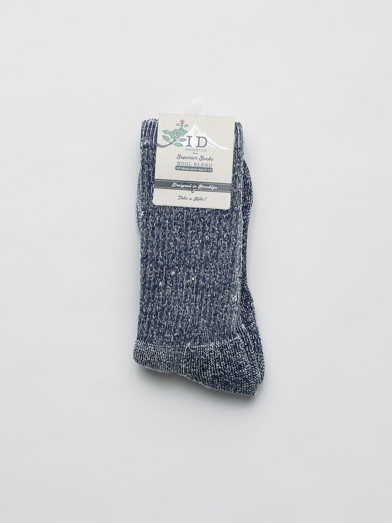ID Menswears Merino Wool Blend Socks, in dark blue speckled design with a cream label adorned with a minimal floral logo and text, are renowned for their breathability and cold-weather comfort. The socks are neatly folded and displayed on a plain white background.