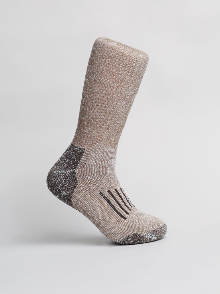 A single sock from ID Menswears Merino Wool Blend Socks stands upright, beige in color with a reinforced heel and toe for cold-weather comfort. It features a textured fabric reminiscent of Merino wool, with dark stripes on the sole against a white background.