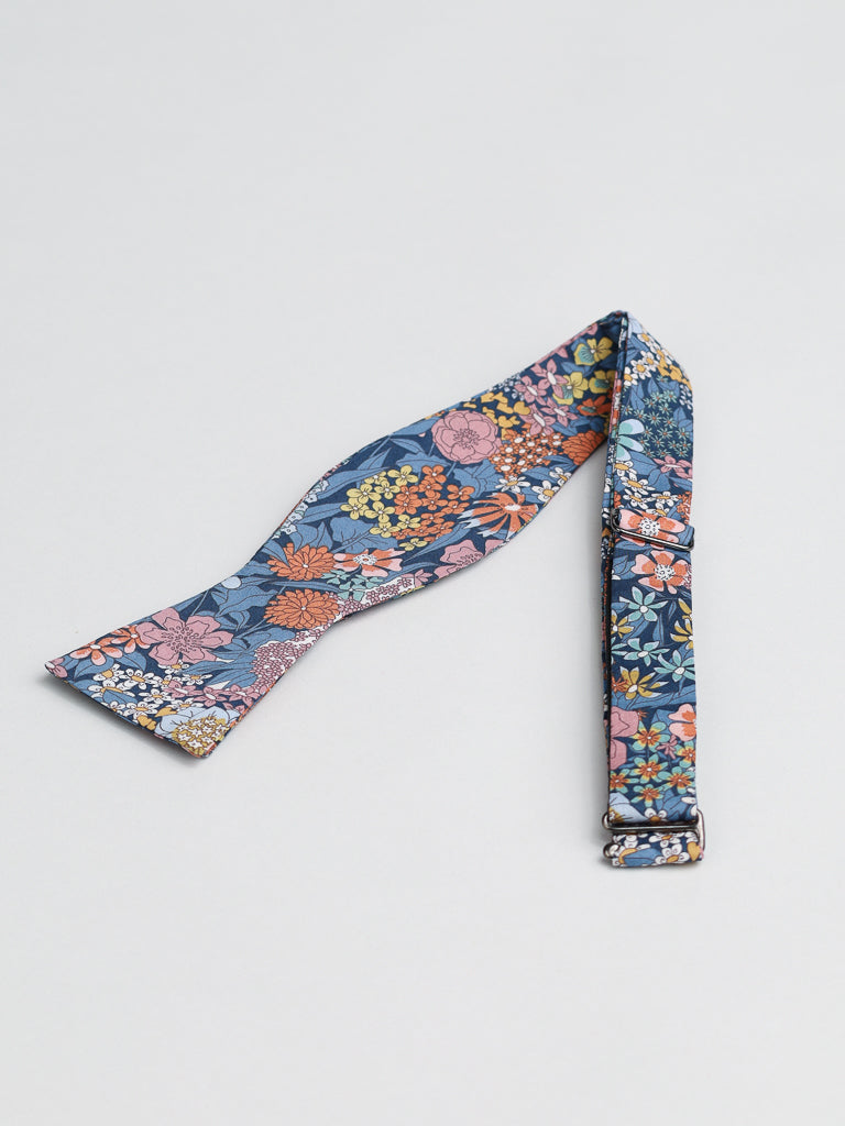 The Liberty of London Tana Lawn™ Ciara Bowtie by ID Menswear is a blue self-tie bow tie, handmade in Brooklyn from luxurious cotton, featuring a colorful floral pattern with pink, orange, yellow, and green flowers.
