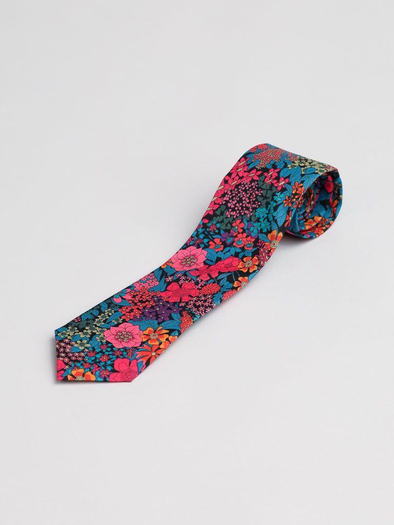The ID Menswear Liberty of London Tana Lawn™ Ciara Tie, showcasing a vibrant floral print in pink, red, orange, blue, and green, is rolled and displayed on a plain white background.