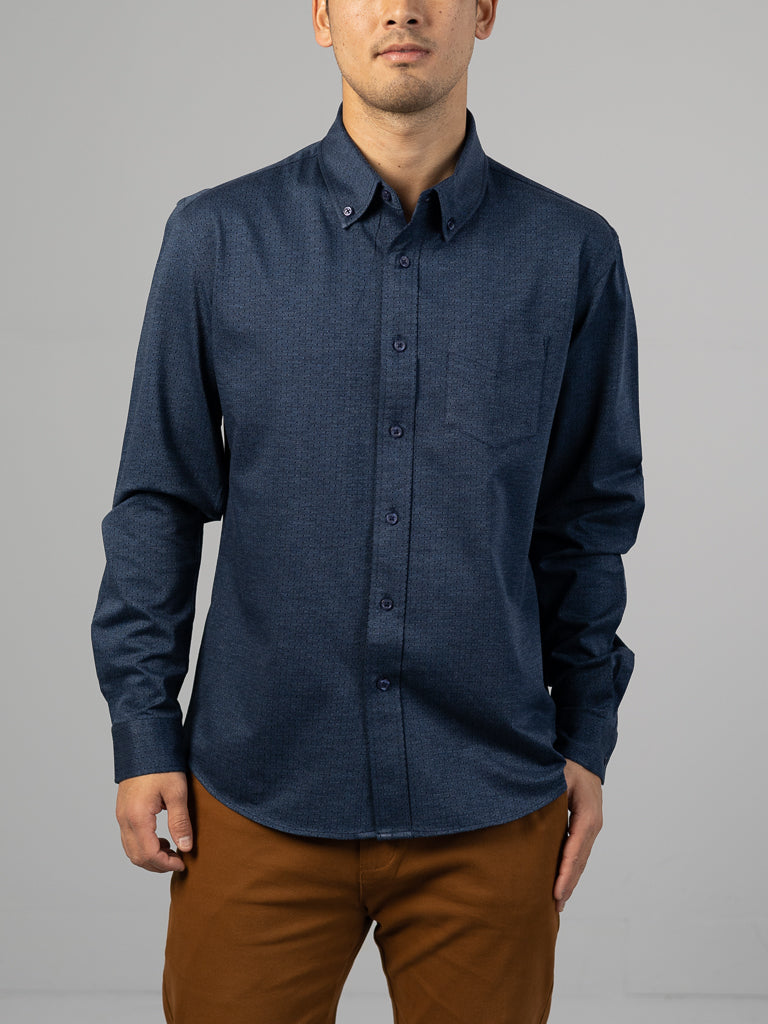Against a gray background, someone wears ID Menswears Leo Stretch Button Down Shirt in dark blue, featuring a left chest pocket and comfortable stretch, paired with brown pants.