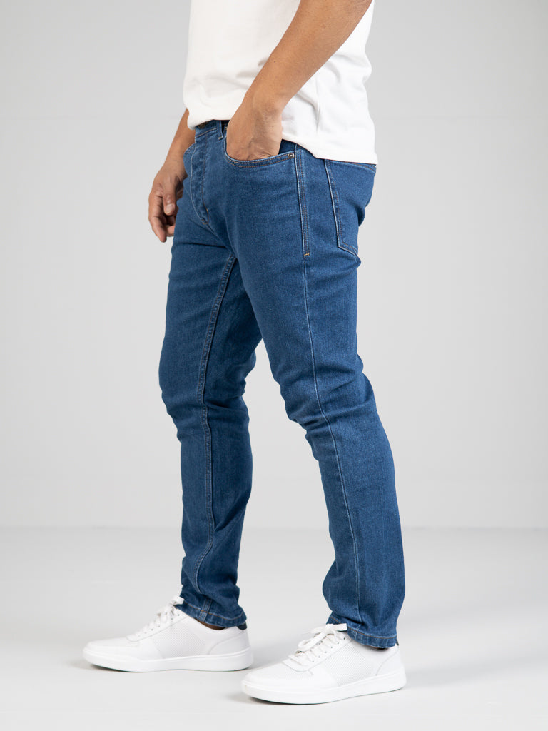 A person stands with hands in pockets against a plain background, wearing a white t-shirt, ID Menswears Ganbaru Stretch Jean with a slim-tapered fit, and white sneakers.