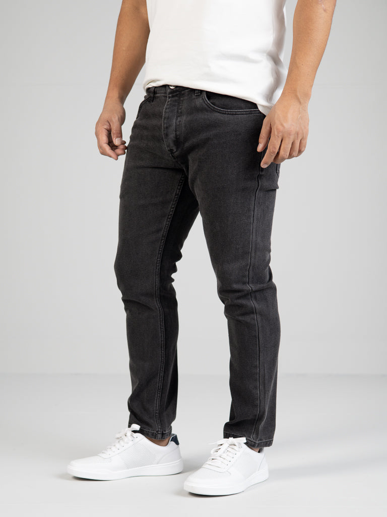 Against a plain background, someone wears an ID Menswear white t-shirt, Ganbaru Stretch Jean (slim-tapered), and white sneakers. They stand confidently with one leg slightly forward, shown from shoulders down.