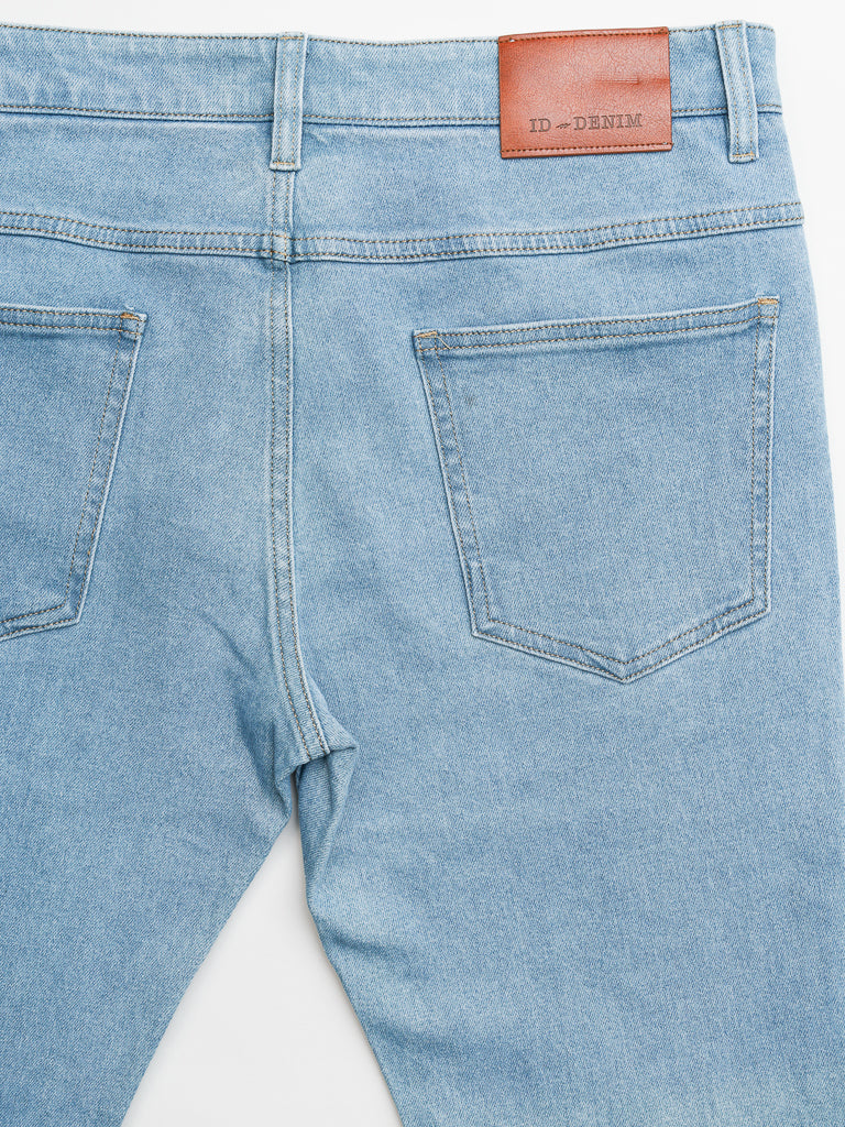 The image displays the back of Ganbaru Stretch Jeans by ID Menswear, featuring a light blue, slim-tapered fit with two pockets and an ID-DENIM brown leather patch on the waistband. These stylish jeans are laid flat on a crisp white background.