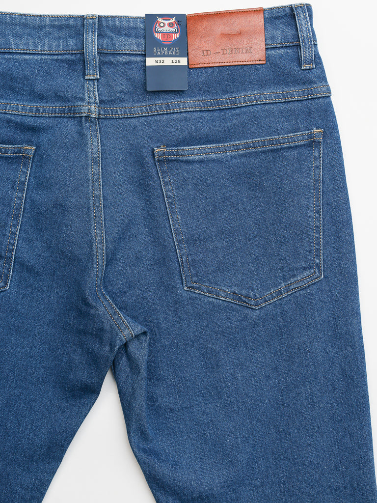 The back of the blue Ganbaru Stretch Jean features two pockets and a leather waistband patch with ID Menswear. A brand tag hangs from the belt loop. Made from cotton twill, these jeans provide a classic yet casual look with a modern slim-tapered fit.