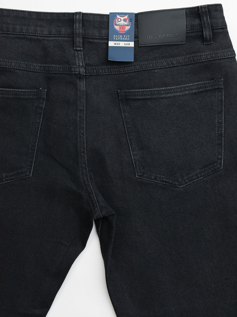 The Ganbaru Stretch Jean by ID Menswear is a black denim piece made from cotton twill. It features a back view with two pockets, a leather patch, and a blue tag with a stylized face. The waistband indicates W32 L28, and its slim-tapered fit ensures both style and comfort.
