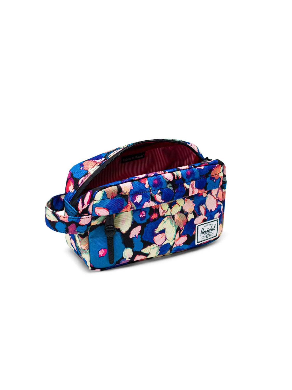 The Herschel Chapter Travel Kit is a rectangular toiletry bag with a blue background, colorful floral pattern, side handle, waterproof zipper, white Herschel label on the front, and a red and white striped interior lining.