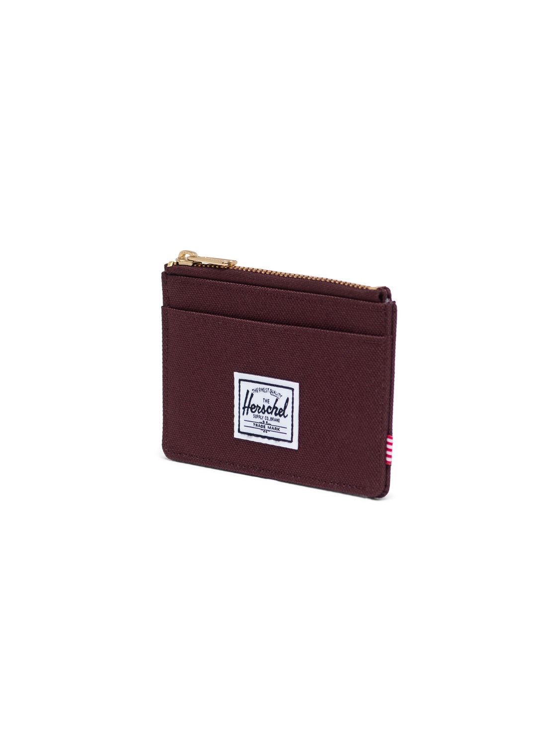 The Herschel Oscar Compact Wallet is maroon with a white logo patch on the front. This zippered card holder has a gold top zipper, side pocket, and is shown on a plain white background.