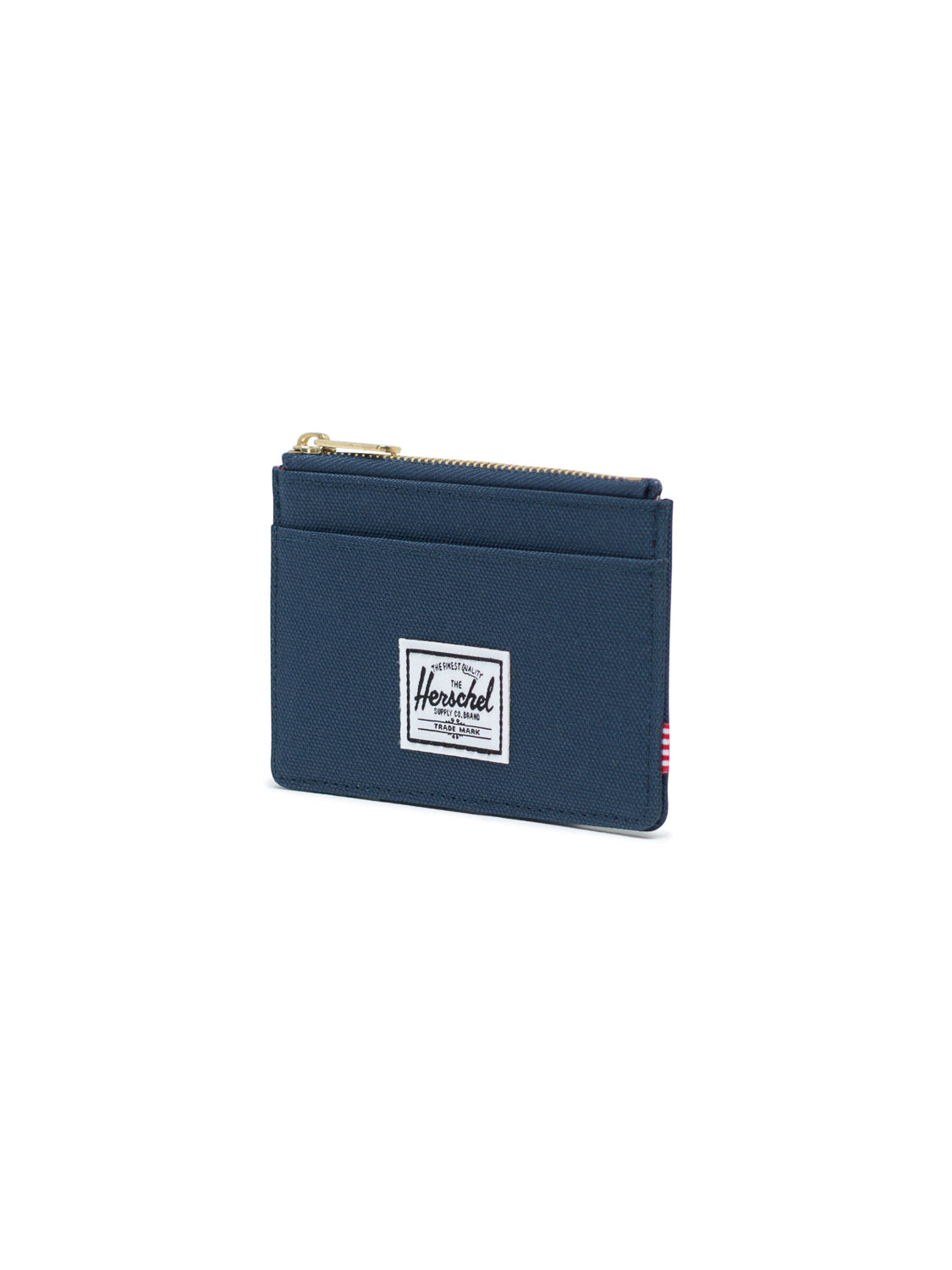 The Oscar Compact Wallet by Herschel is a slim, navy blue card holder with a top zipper, exterior pocket, and a white rectangular Herschel label on the front. It’s displayed against a white background.