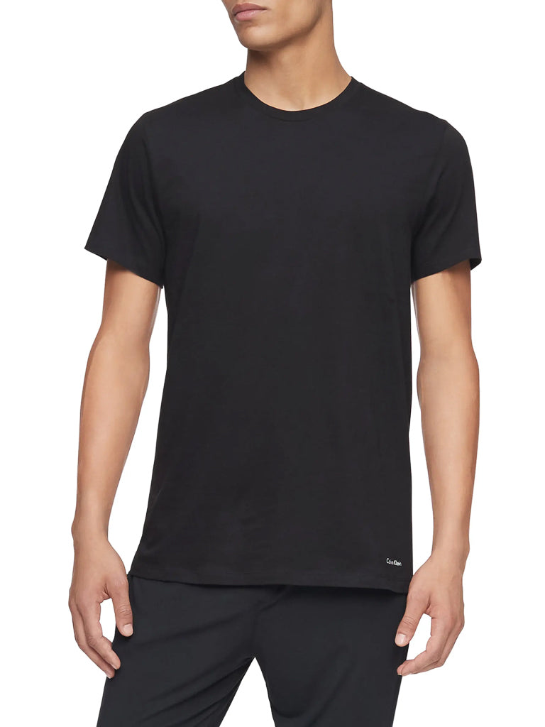 A person wearing a Calvin Klein NB4051 Cotton Classic Crewneck Tee in black, paired with black pants, stands against a white background with arms relaxed at their sides.