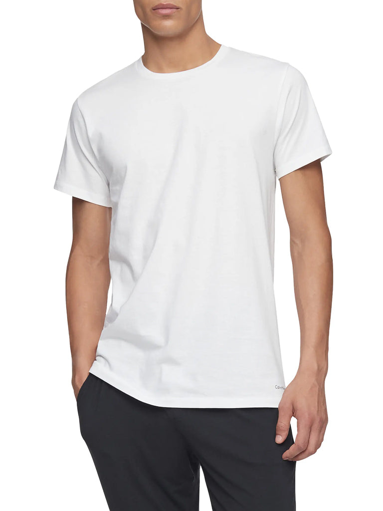 A person stands with one hand in their pocket against a white background, wearing black pants and a Calvin Klein NB4051 3-Pack Cotton Classic Crewneck Tee by Calvin Klein.