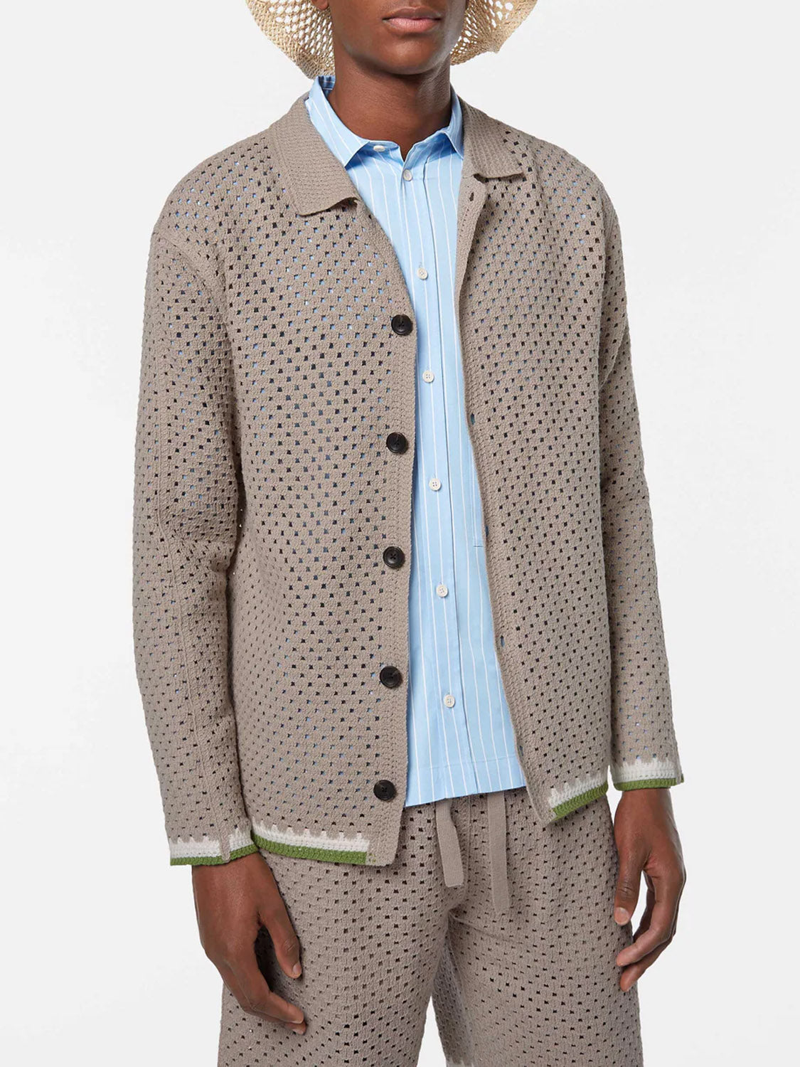 A person models the SCOTCH AND SODA Crochet Long Sleeve Shirt 180084 SU25 in beige, layered over a light blue striped shirt with matching crochet pants and a woven hat—an artistic look perfect for creative settings. Upper body to mid-thigh view shown.