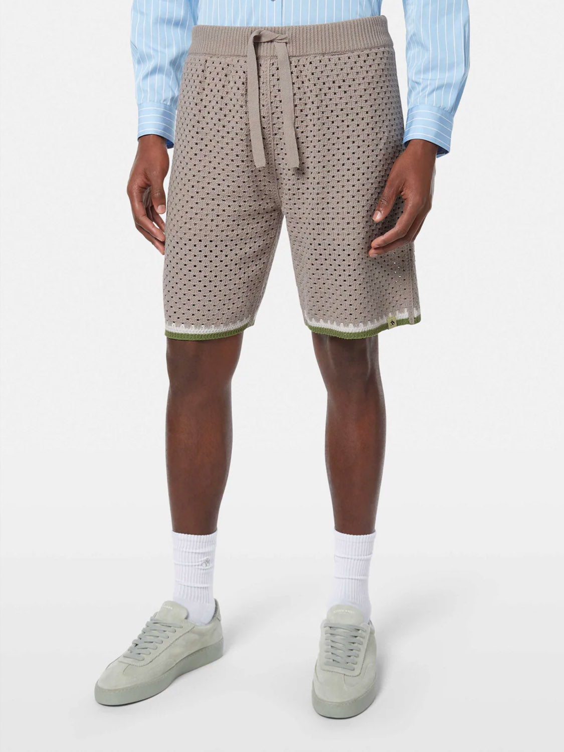 A person wearing SCOTCH AND SODA Crochet Knit Short 180344 SU25 in beige, a light blue striped shirt, white socks, and light gray sneakers stands against a plain white background.