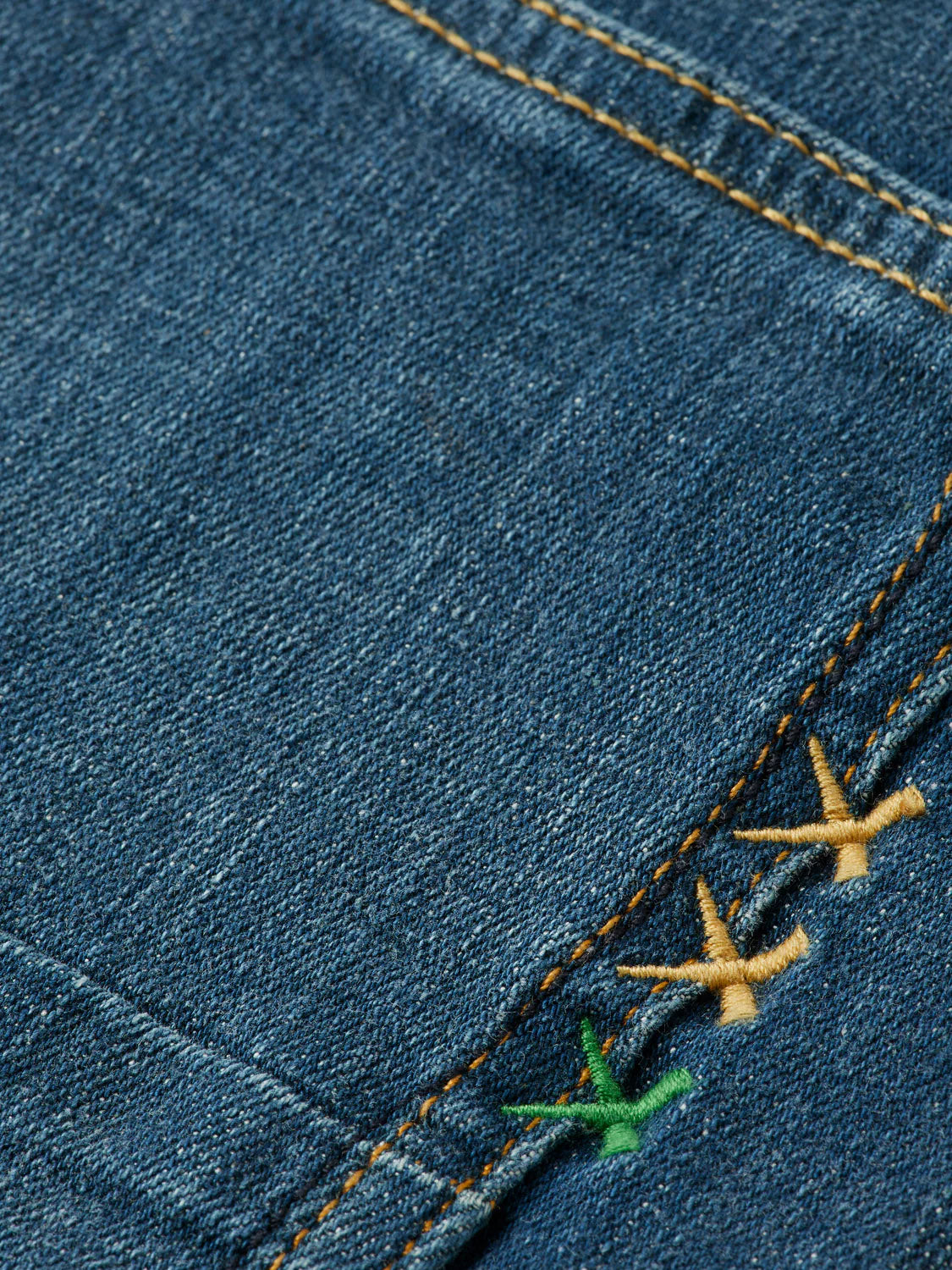 Close-up of 180872 Ralston Regular Slim Denim by Scotch & Soda, featuring blue denim with orange stitching and three decorative cross-stitches in yellow and green on the seam for a detailed, stylish finish.