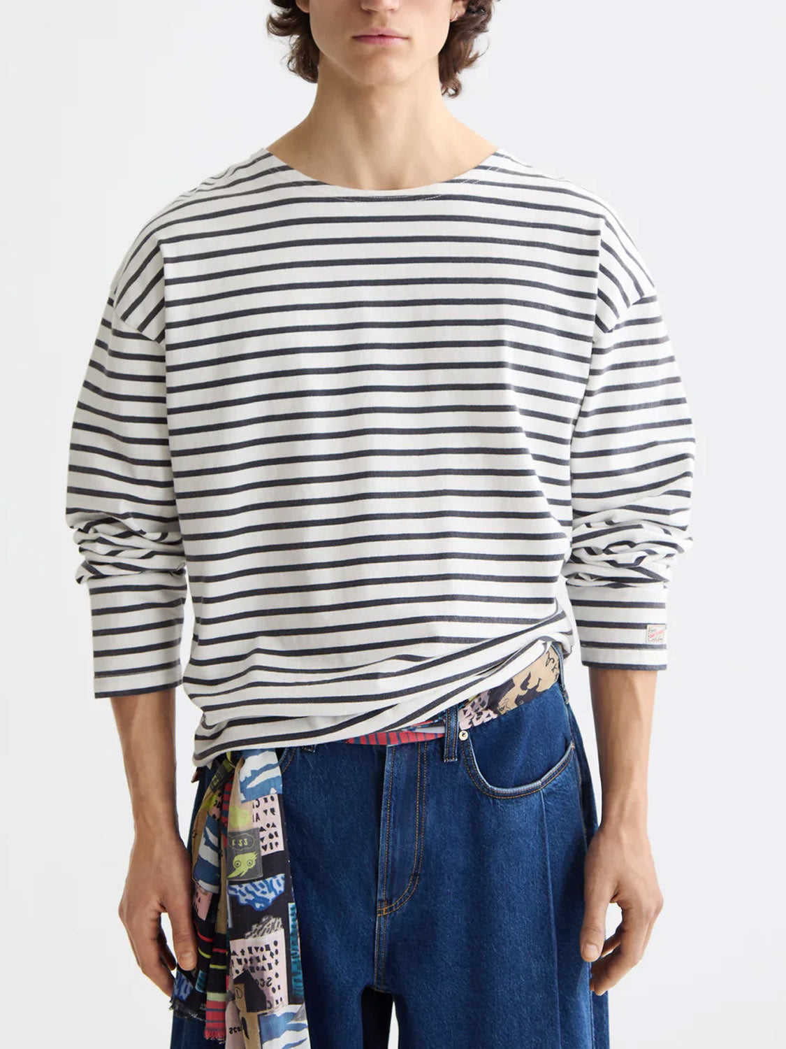 A person wearing the Scotch &amp; Soda 180878 Denim Washed Long Sleeve Breton Tee with horizontal black stripes, blue jeans, and a colorful patterned belt. The image is cropped at the shoulders and mid-thigh.