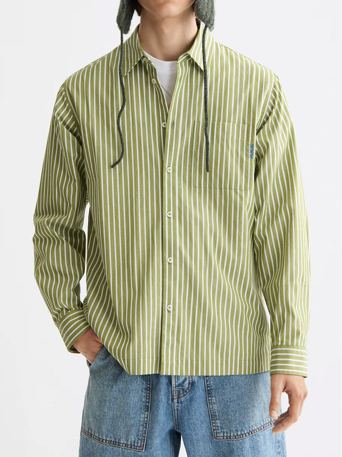 A person wears the Scotch & Soda 181232 Striped Poplin Shirt in green and white, paired with blue jeans and a gray knit hat with ear flaps; only their lower face is visible.