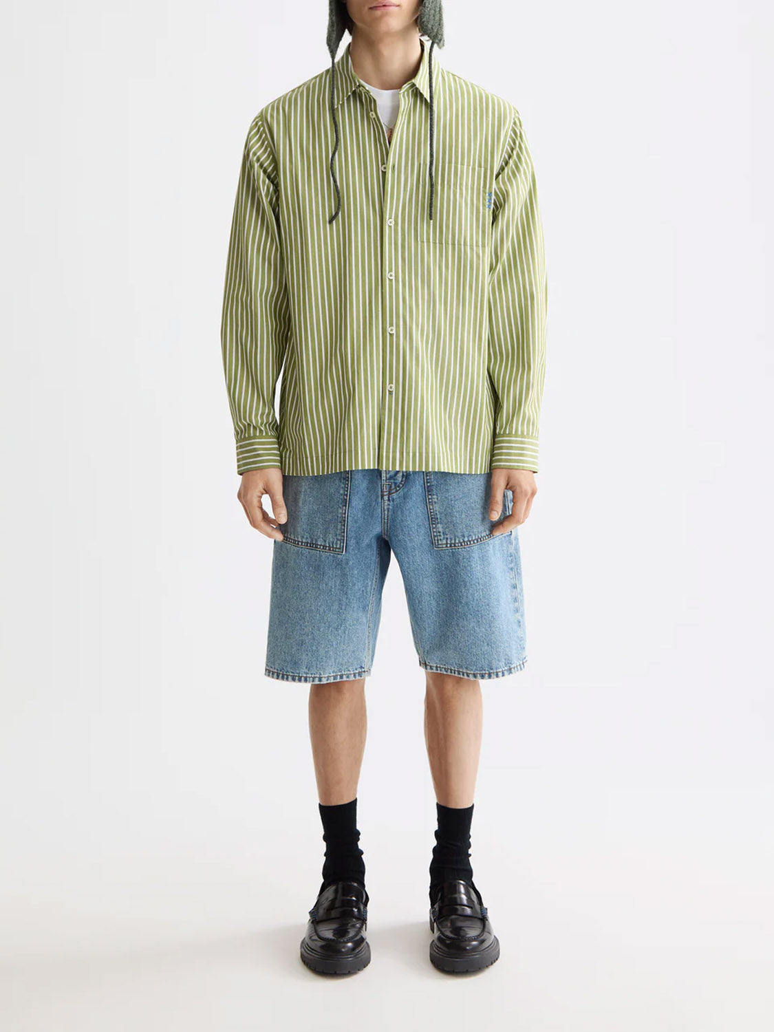 A person wearing a Scotch & Soda 181232 Striped Poplin Shirt, light blue knee-length denim shorts, black socks and shoes, and a green knit hat with strings stands against a plain light background.