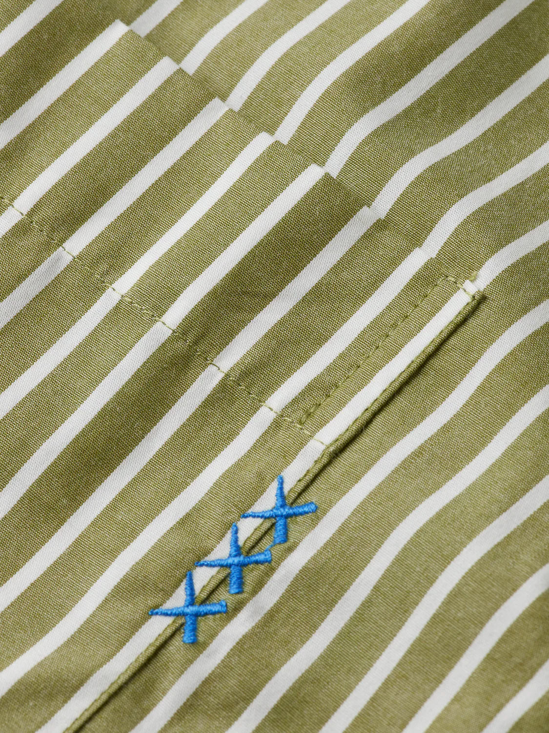 Close-up of the Scotch & Soda 181232 Striped Poplin Shirt in green and white, relaxed fit, 100% cotton, with a pocket and three blue embroidered X stitches by the seam.