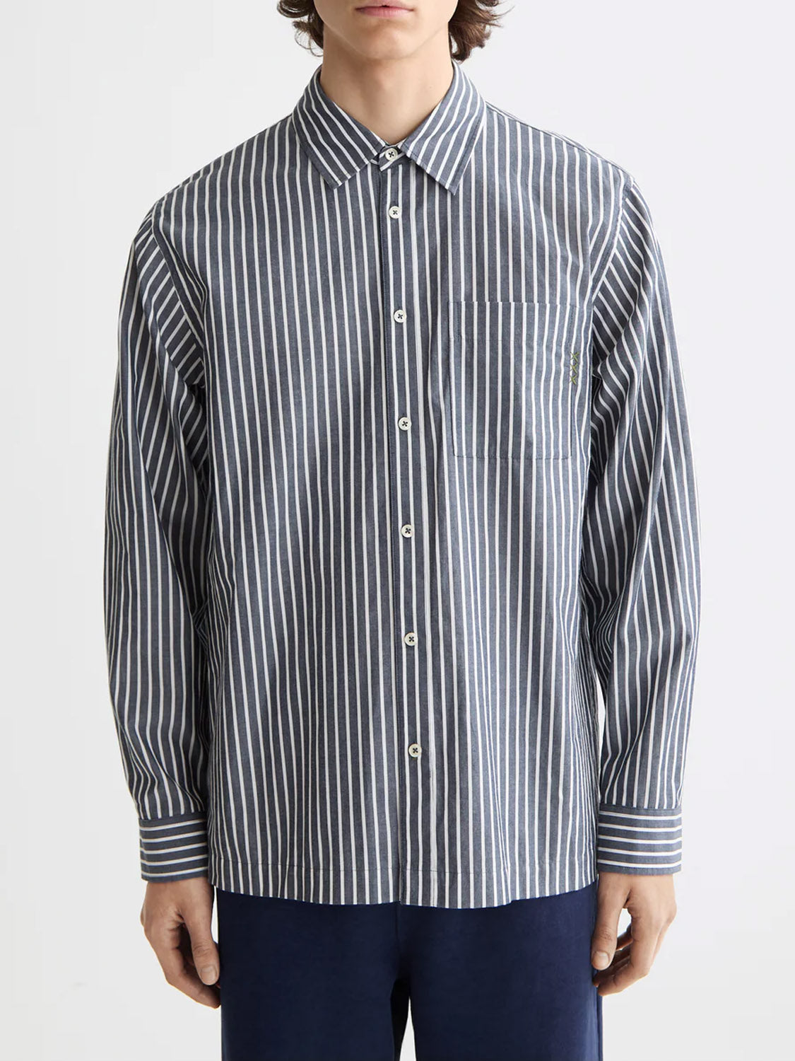 A person wears the Scotch & Soda 181232 Striped Poplin Shirt—relaxed-fit, 100% cotton with vertical navy and white stripes, a collar, and chest pocket—standing against a plain light background.