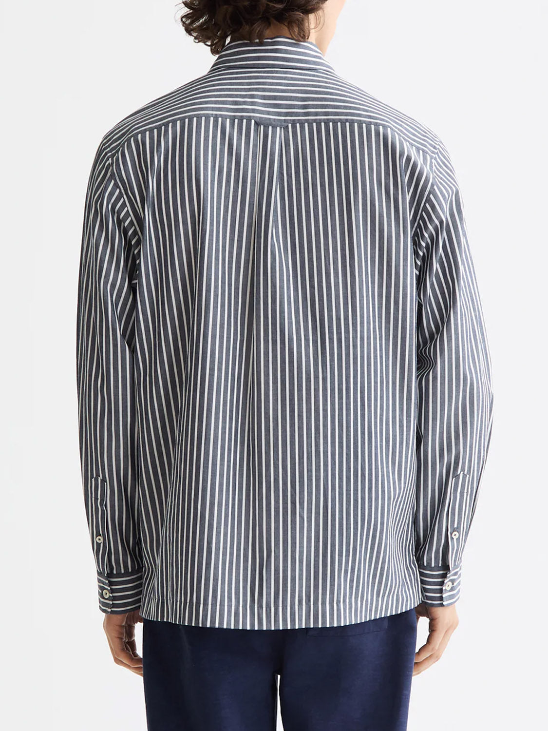 A person is seen from behind wearing the Scotch & Soda 181232 Striped Poplin Shirt—100% cotton, relaxed fit, with vertical black and white stripes—paired with dark pants against a plain white background.