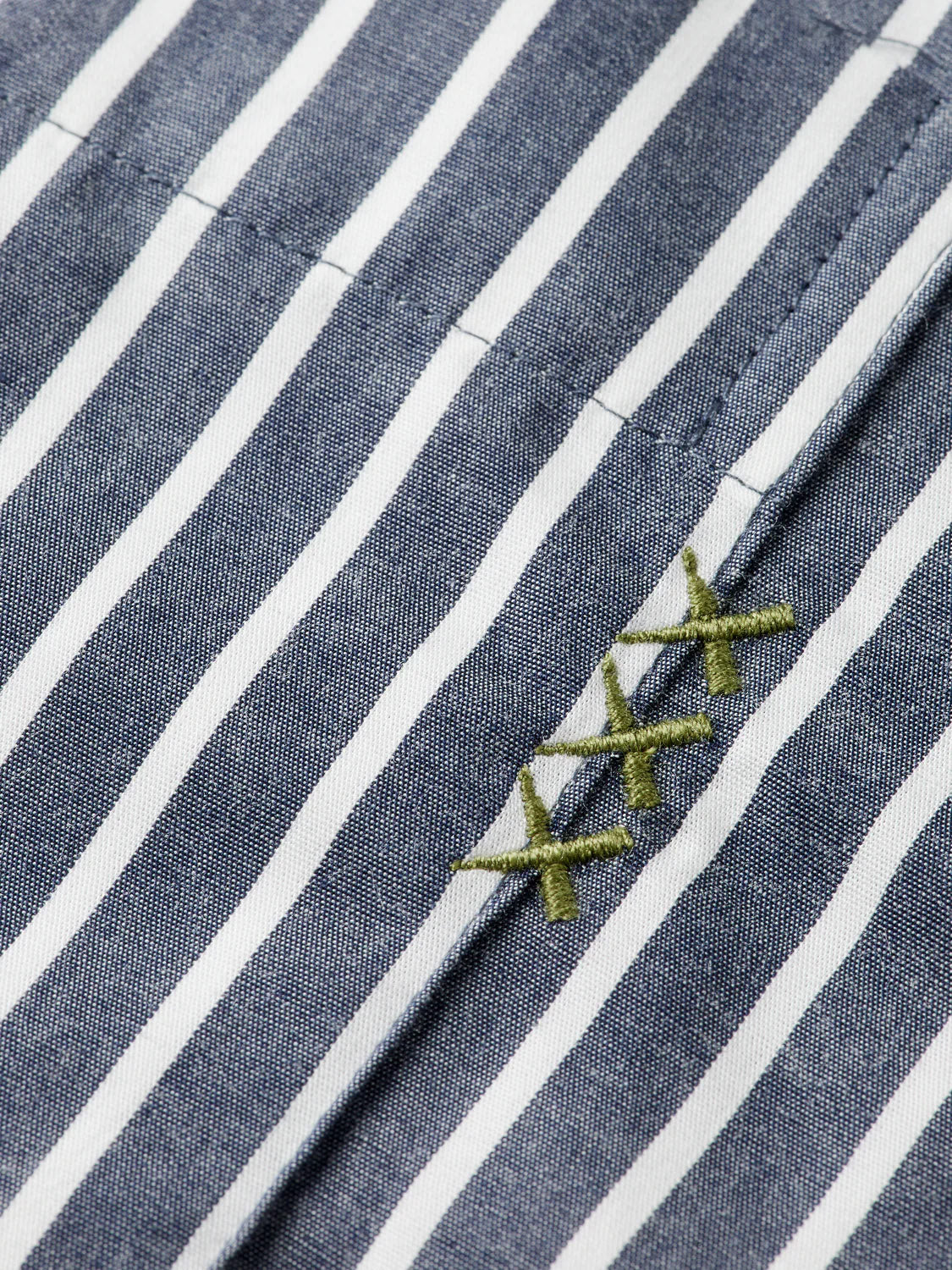 Close-up of blue and white vertical striped fabric from Scotch & Soda’s 181232 Striped Poplin Shirt, made from 100% cotton, with three green X-shaped stitches embroidered diagonally on one stripe.