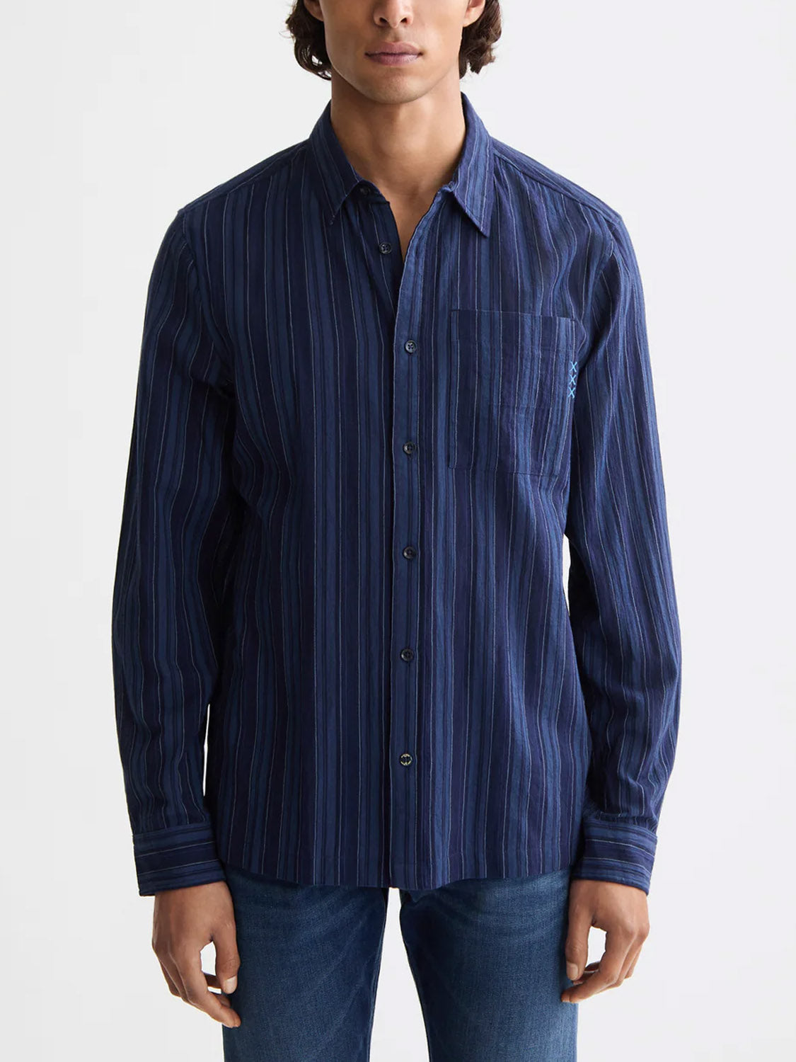 A person wears the Scotch & Soda 181248 Textured Stripe Shirt, a long-sleeve indigo striped button-up with chest pocket, paired with blue jeans, standing facing forward against a plain light background.