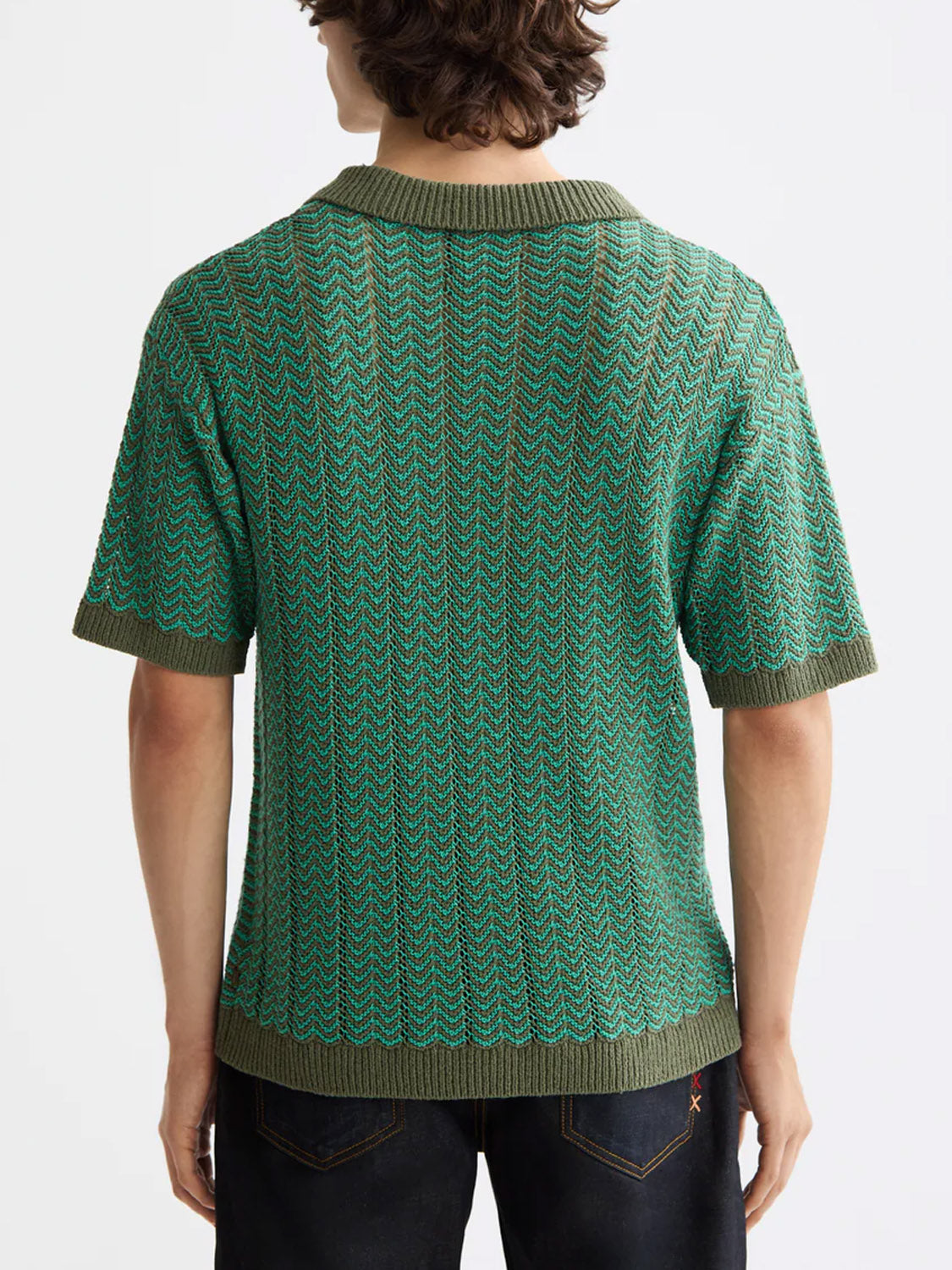 A person with medium-length brown hair is seen from the back wearing the Scotch & Soda 181322 Open Structured Knitted V-Neck Polo in green, paired with dark blue jeans.